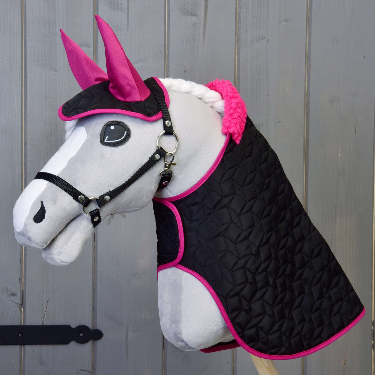 Hobby Horse gris avec licol noir portant la couverture matelassée noire à col en fourrure rose et le bonnet d'oreilles aux oreilles roses
