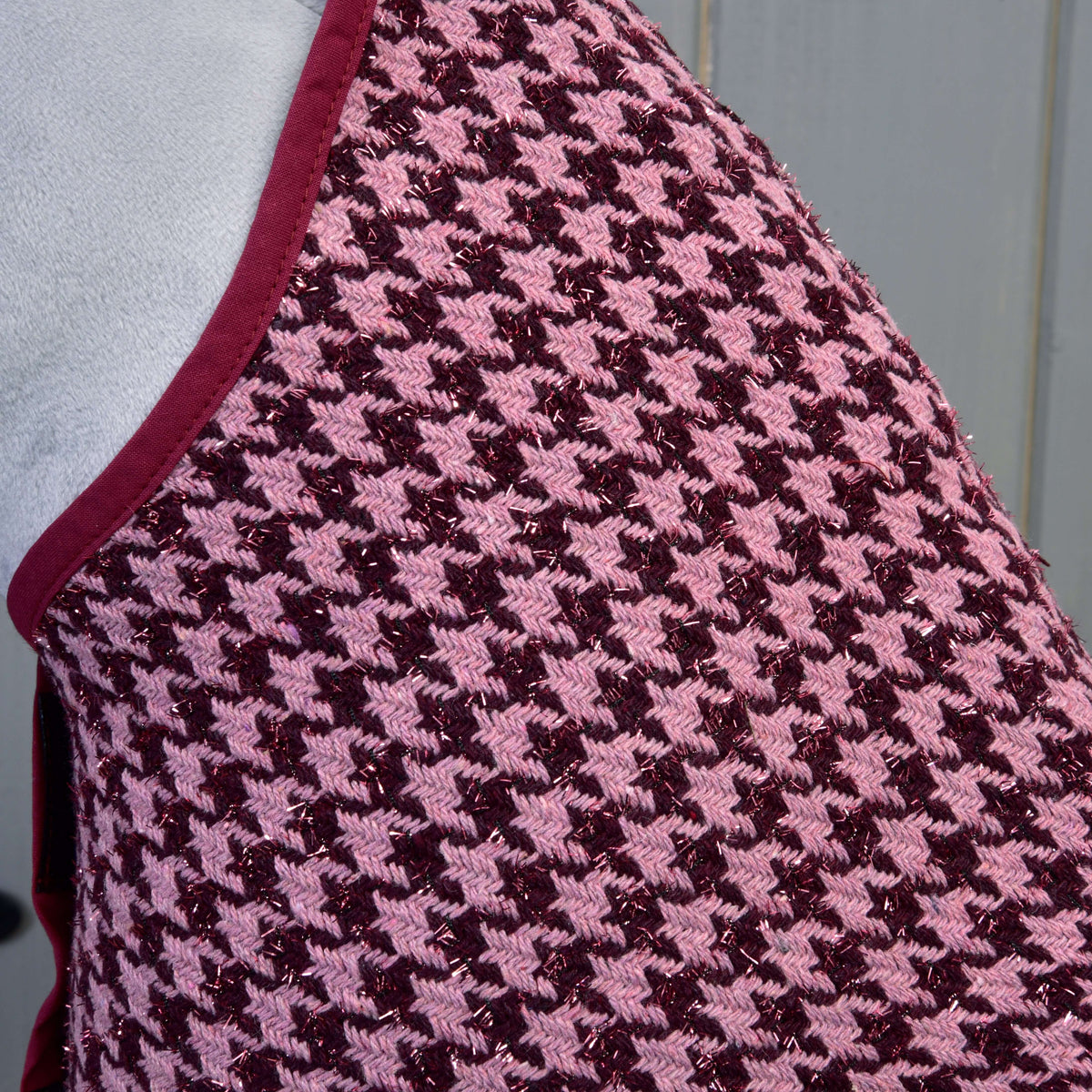 Close-up van de dekenstof met pied-de-poule in roze en bordeaux met glinsterdraad en bordeauxrode bies