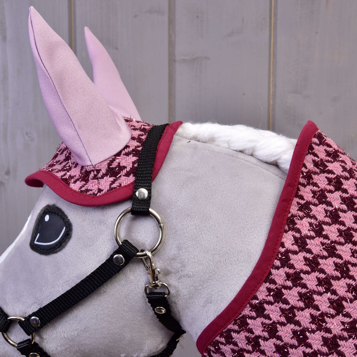 Close-up van het oornetje met pied-de-poule en lichtroze oren en de bordeauxrode bies van de deken op een grijze Hobby Horse