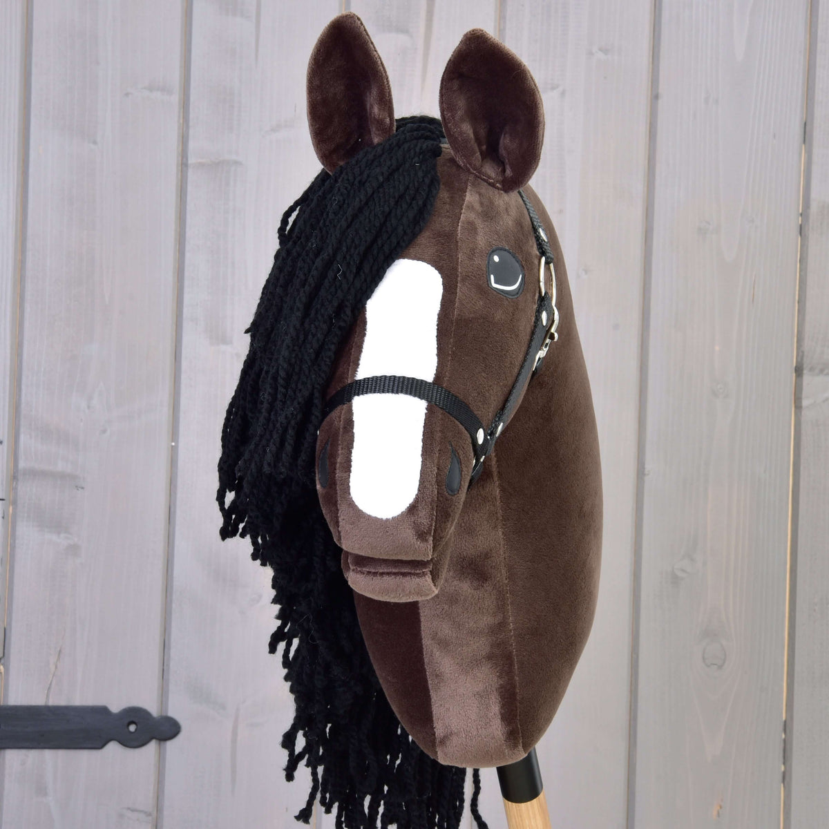 Vooraanzicht van de donkerbruine Hobby Horse Sisi met witte bles, zwarte voorlok van garen en zwarte halster
