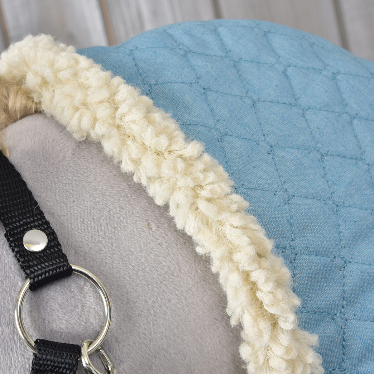Crèmekleurige fleecerand van de staldeken Sky Blue op een grijze Hobby Horse, naast de zwarte halster met zilveren ring