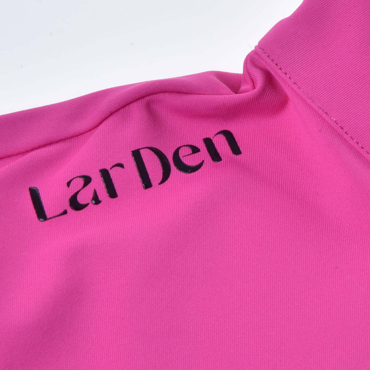Close-up of black LarDen lettering on the shoulder of the bright pink Hobby Horse T-Shirt, next to the collar