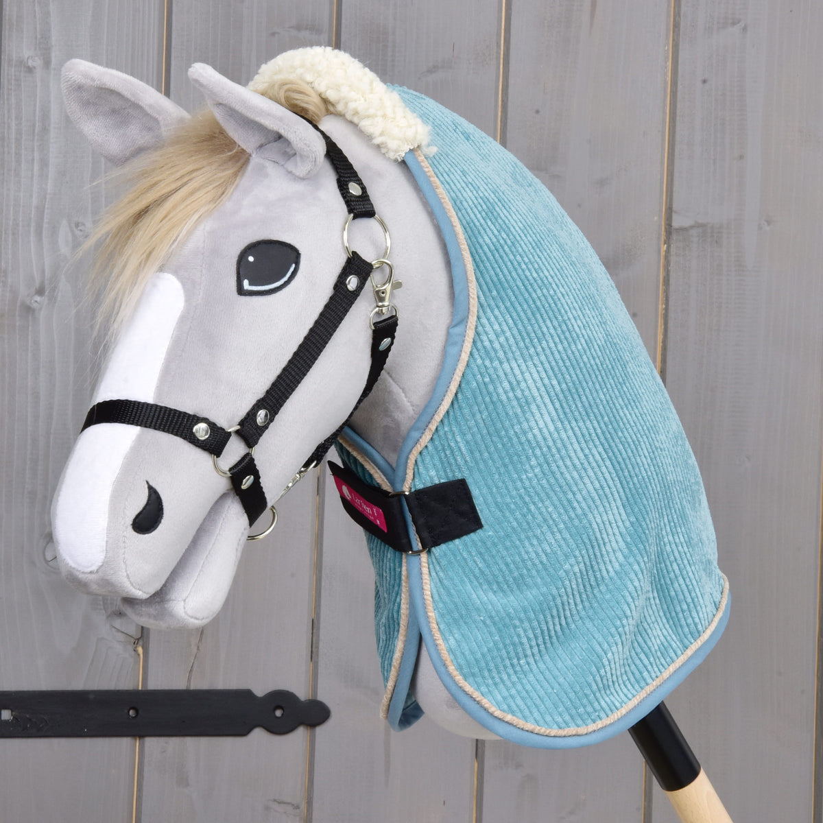 Lichtgrijze Hobby Horse met zwart halster in de petrolblauwe ribfluwelen staldeken met crèmekleurige teddykraag