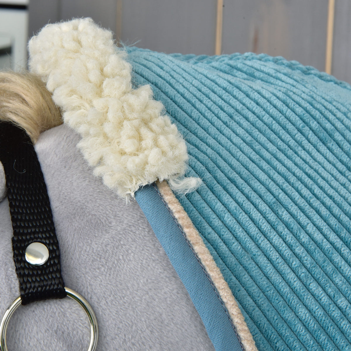 Close-up van de gekrulde crèmekleurige teddykraag op de petrolblauwe ribfluwelen deken met blauwe rand en beige bies
