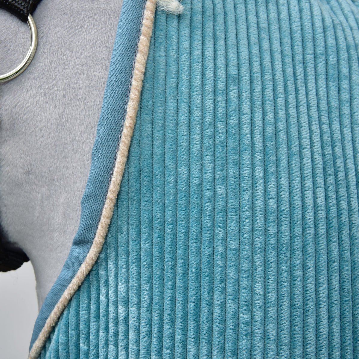 Close-up van de brede petrolblauwe ribbels met blauwe rand en beige bies langs de zoom bij de ring van het halster