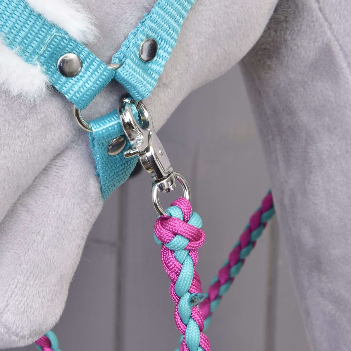 Close-up of a braided pink and turquoise rope hanging from the snap hook of the turquoise webbing halter