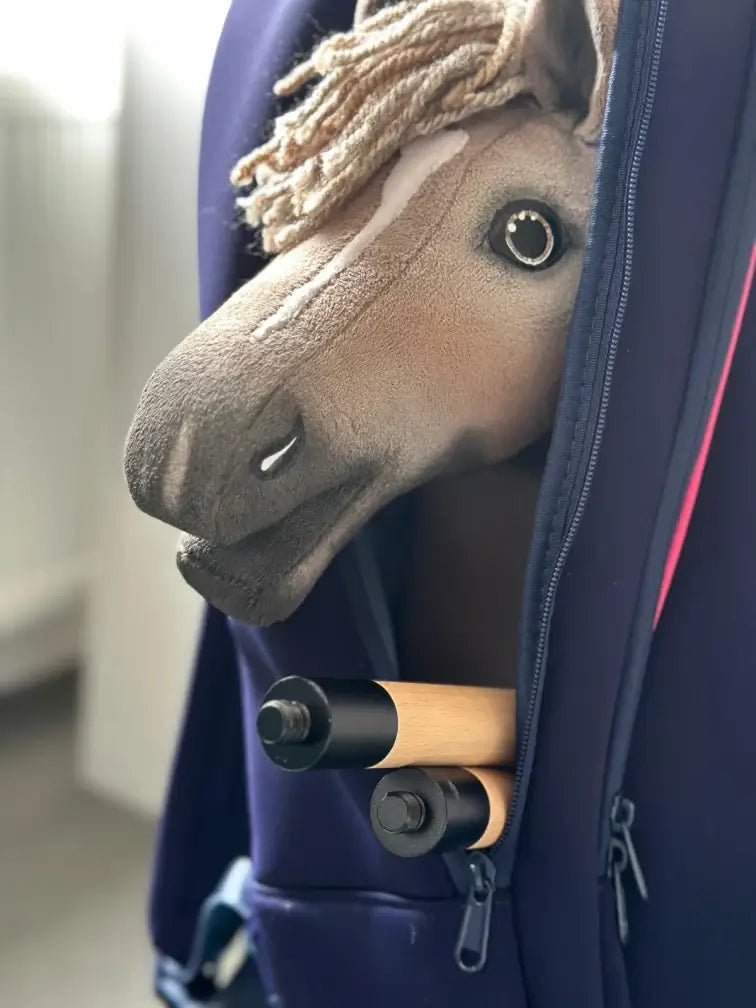 Hobby Horse brun clair à crinière beige en fil sortant d’un sac à dos bleu marine à côté d’un bâton en bois en deux parties