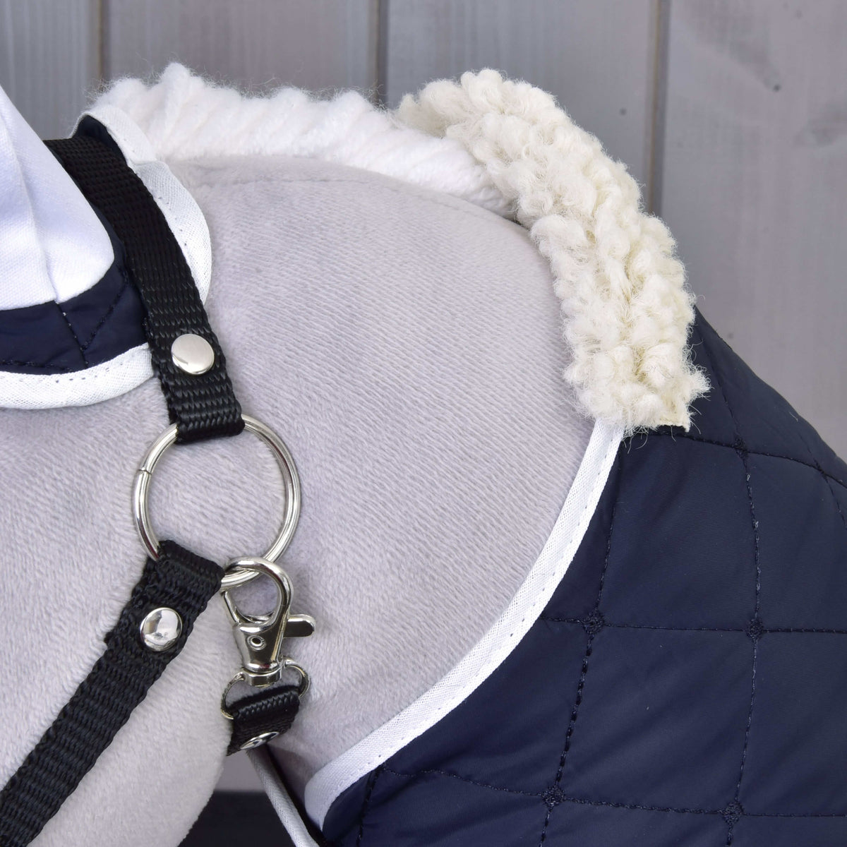 Gros plan sur le col polaire crème et la couverture matelassée bleu marine bordée de blanc sur un Hobby Horse gris