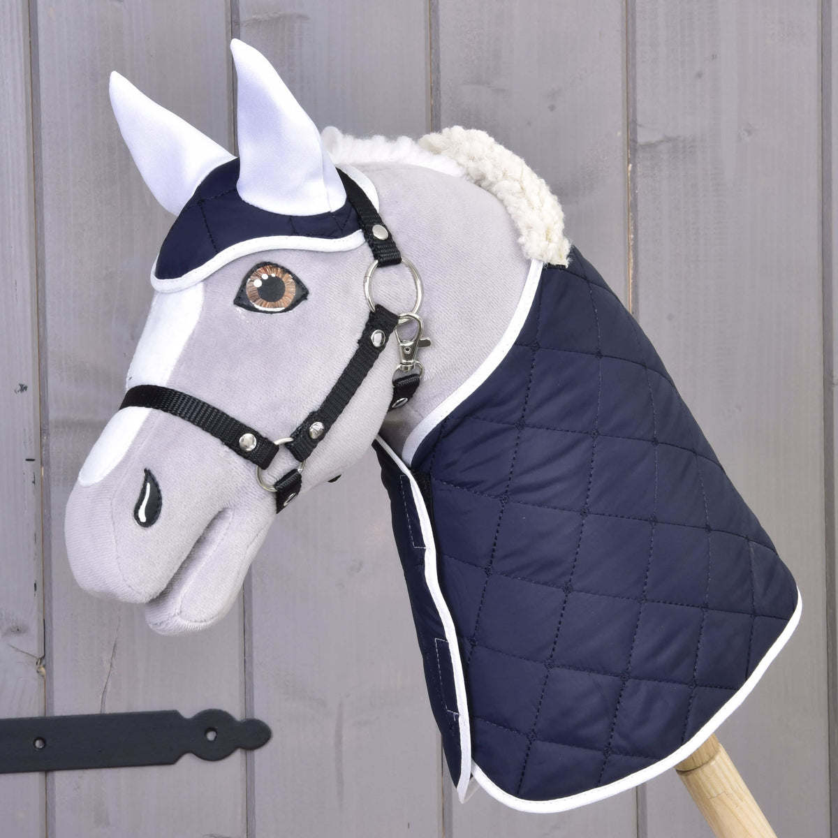 Hobby Horse gris avec licol noir portant la couverture matelassée bleu marine bordée de blanc et le bonnet d’oreilles assorti