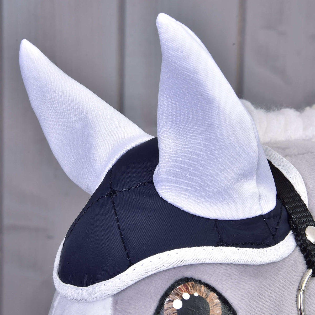 Gros plan sur le bonnet d’oreilles matelassé bleu marine avec oreilles et bordure blanches sur un Hobby Horse gris