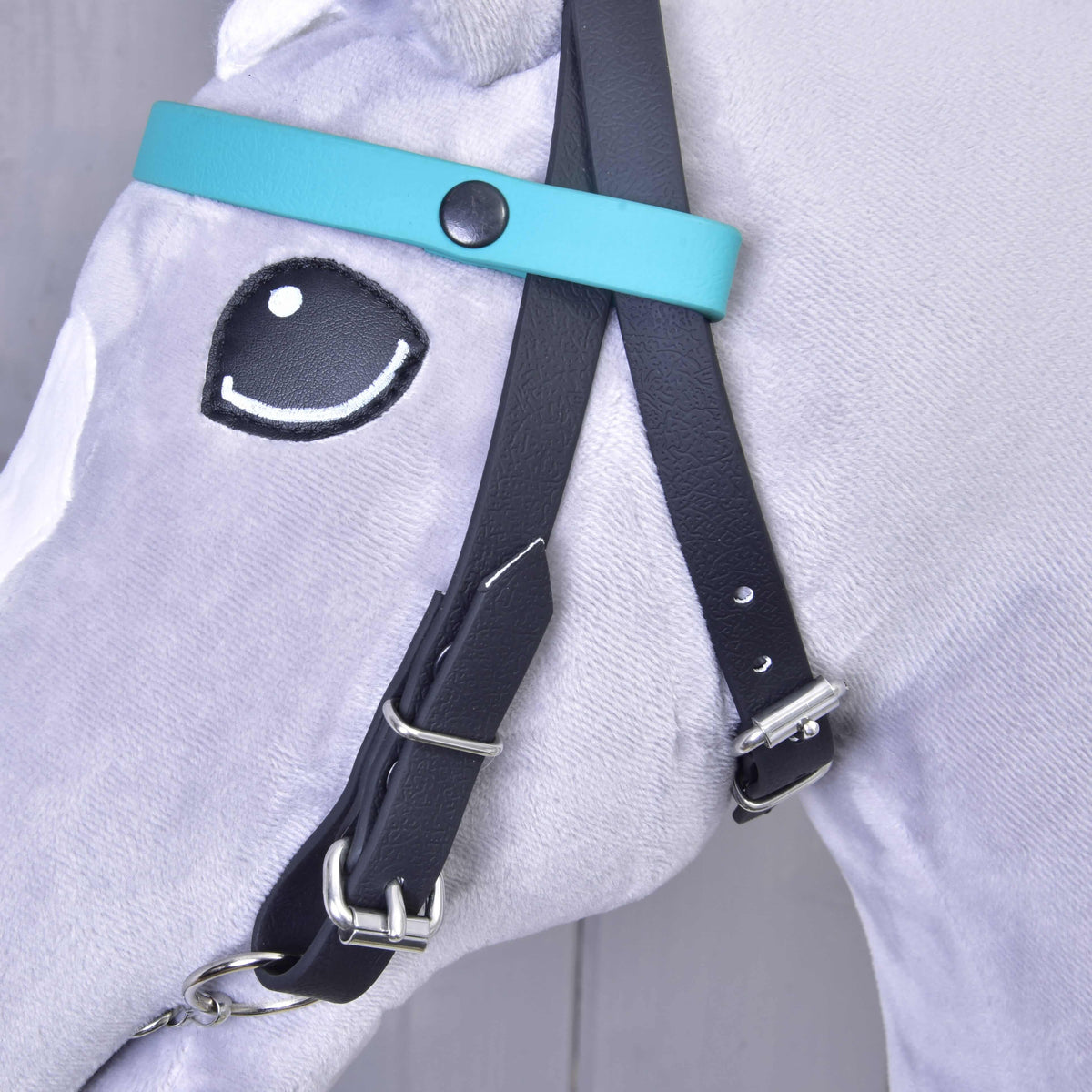 Gros plan sur le bandeau turquoise uni à bouton-pression noir, sur la bride noire d'un Hobby Horse gris
