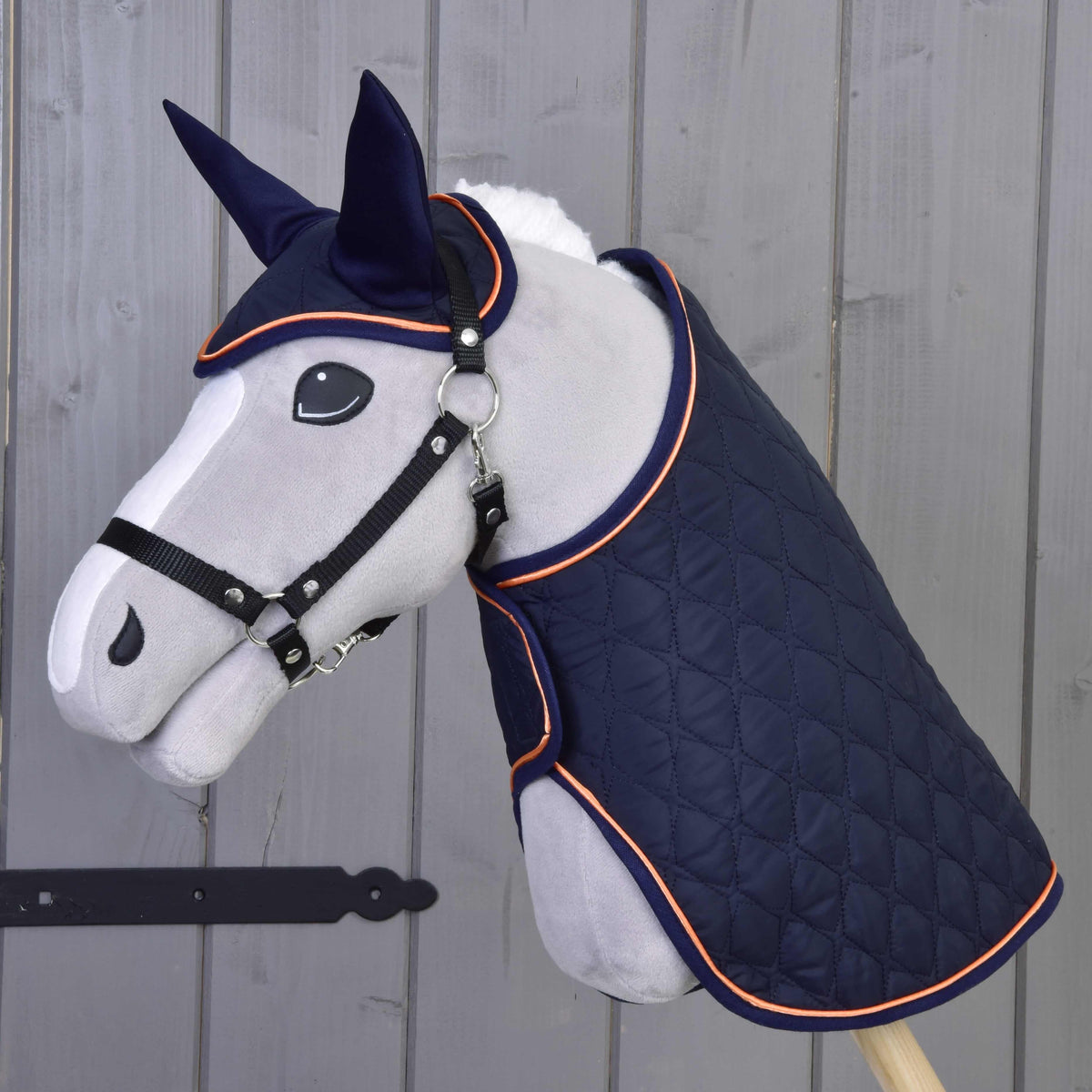 Hobby Horse gris avec licol noir portant la couverture matelassée bleu marine et le bonnet d’oreilles à passepoil orange