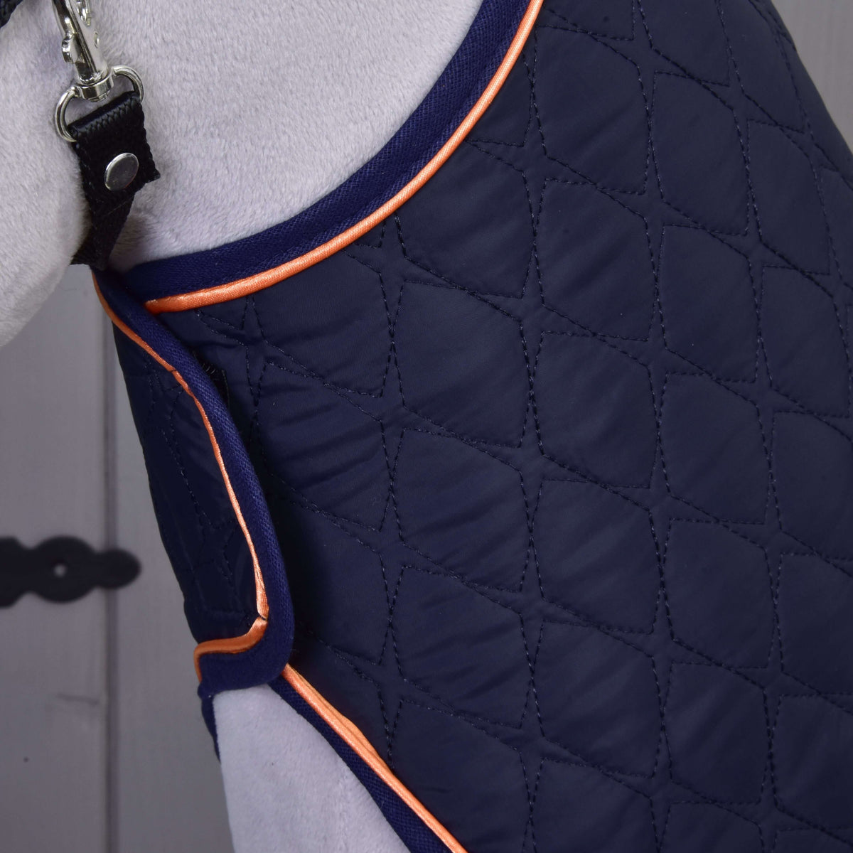 Gros plan sur la couverture bleu marine matelassée en losanges avec passepoil orange autour de l’encolure d’un Hobby Horse gris