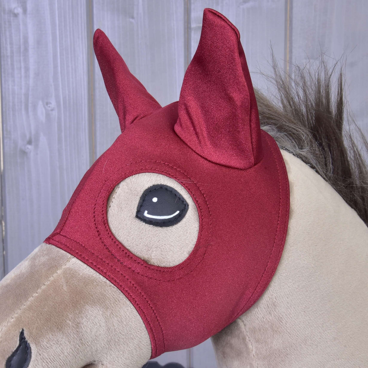 Close-up van het donkerrode masker Barn Red op een beige Hobby Horse, beide oren in puntige oorkapjes en het oog omrand met stiksels