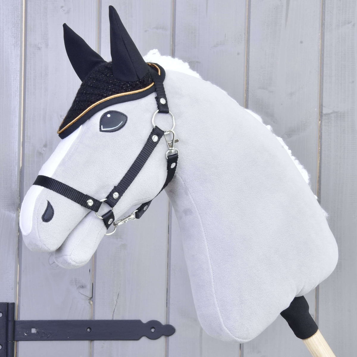 Hobby Horse gris avec licol noir et crinière en fourrure blanche portant le bonnet d’oreilles noir au crochet bordé d’or
