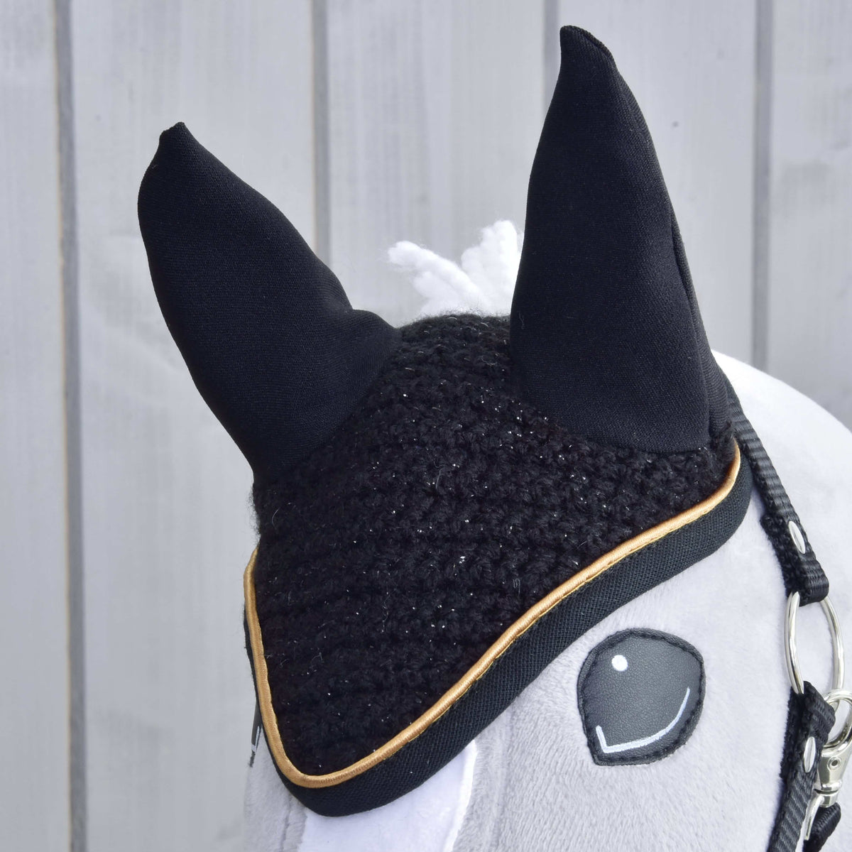 Gros plan sur le bonnet d’oreilles noir au crochet en fil scintillant, oreilles en tissu noir et passepoil doré sur une tête grise
