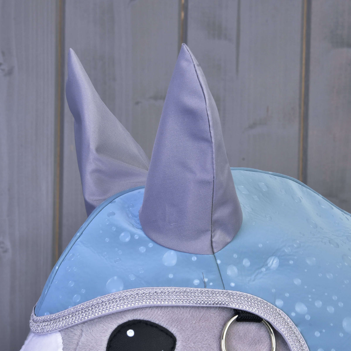 Close-up van de grijze satijnen oren en zilveren glitterbies van de regenjas Blue Drops op een grijze Hobby Horse