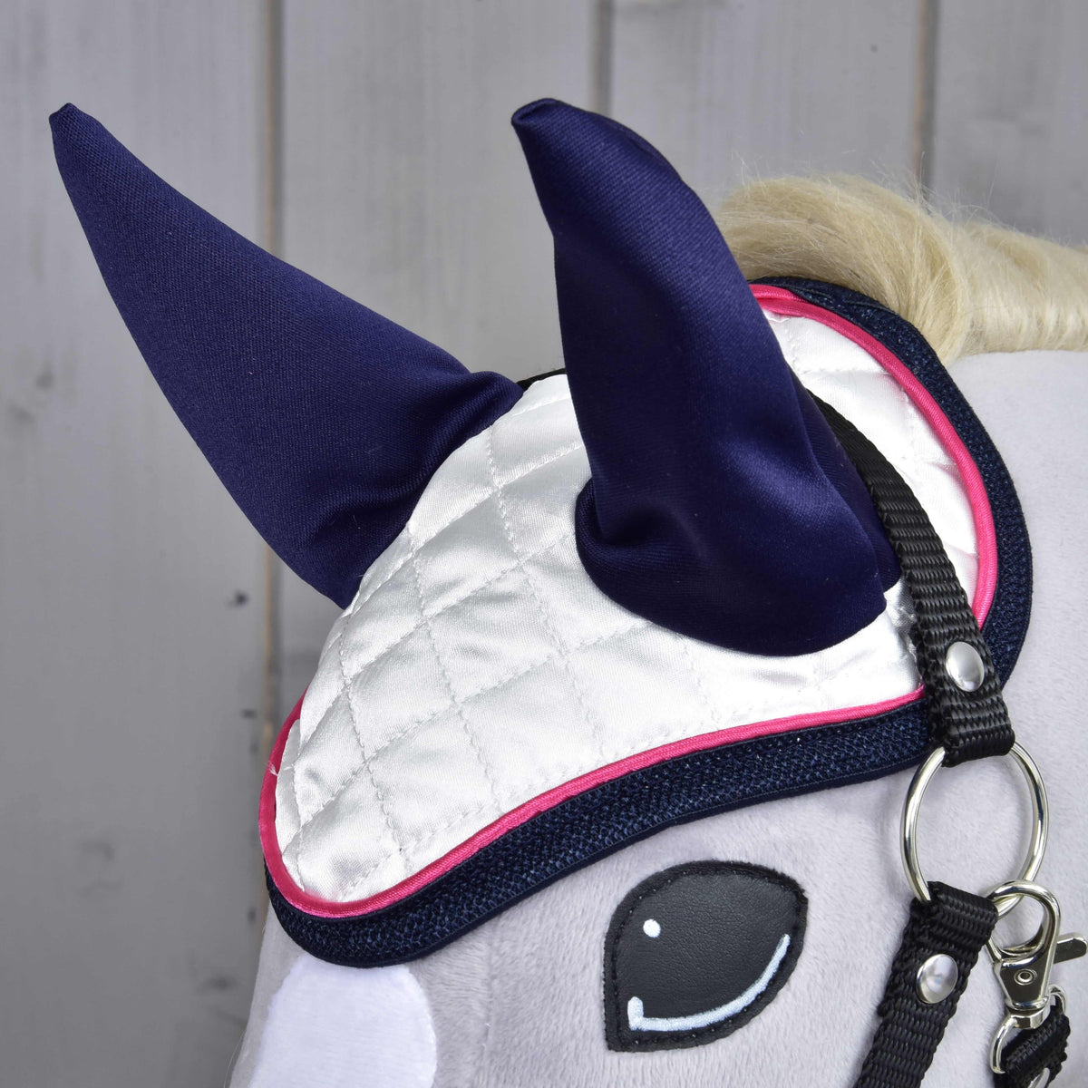Close-up of the white quilted satin ear bonnet with navy ear covers, pink piping and navy binding above the eye