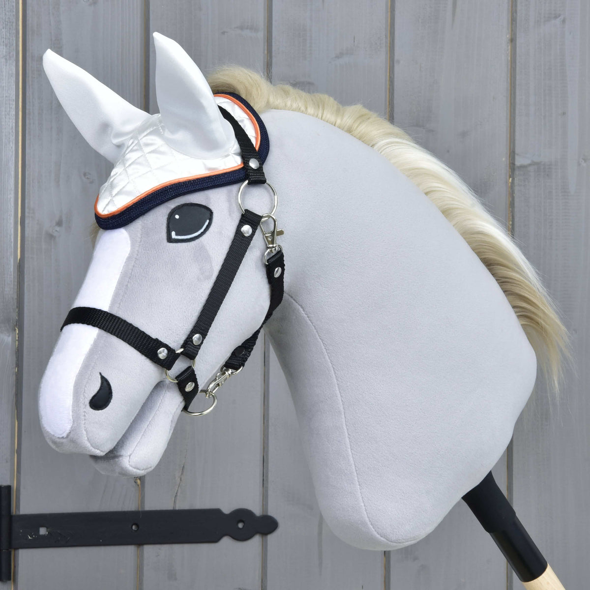 Hobby Horse en peluche grise à crinière crème et licol noir portant le bonnet d’oreilles blanc bordé orange et marine