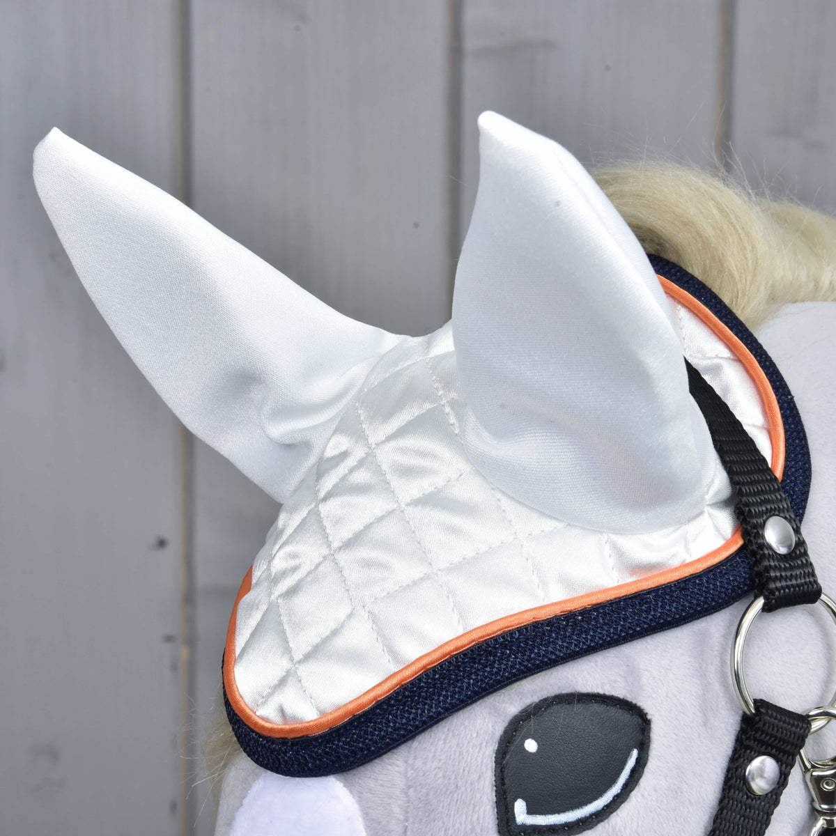 Gros plan sur le bonnet d’oreilles en satin matelassé blanc, passepoil orange et bordure marine au-dessus de l’œil cousu