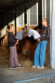 Deux filles dans une écurie avec le Hobby Horse Alfredo et un Hobby Horse gris en imperméables colorés à capuche près d’un cheval bai
