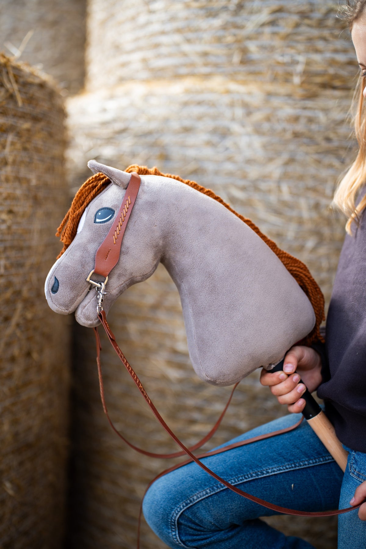 Hobby Horse Chanell de près avec une bride marron à surpiqûres dorées et de longues rênes marron, devant des balles de paille