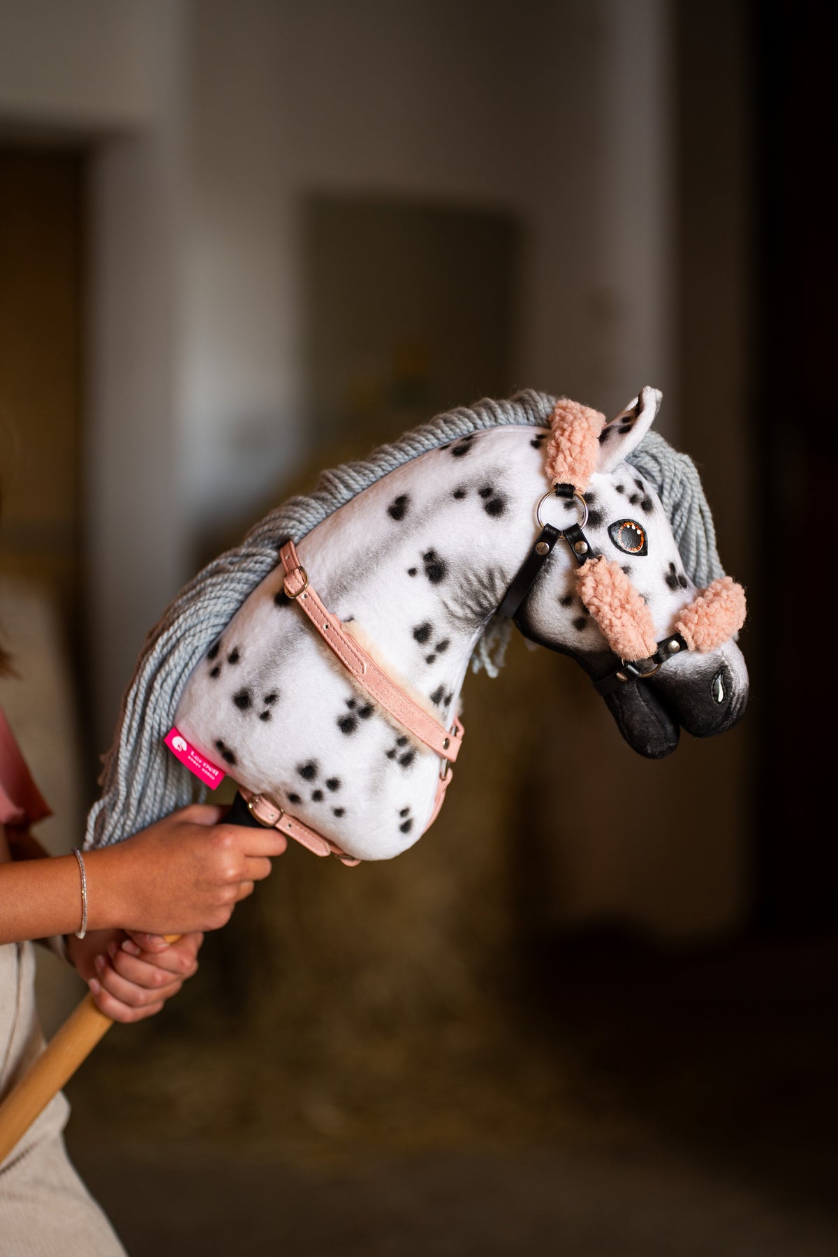 Hobby Horse Chantal de près avec licol à fourrure rose pêche et sangle de poitrail vieux rose, taches noires sur l’encolure blanche