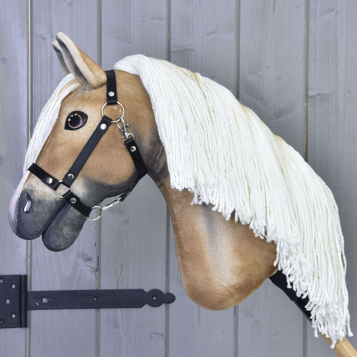 Vue de profil du Hobby Horse fauve doré à longue crinière crème en fil et licol noir, sur un bâton en bois