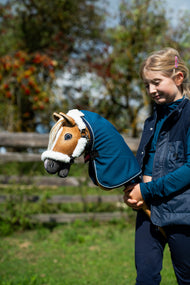 Meisje met de goudbruine Hobby Horse in een petrolblauwe deken en halster met wit bont, herfstbessen op de achtergrond