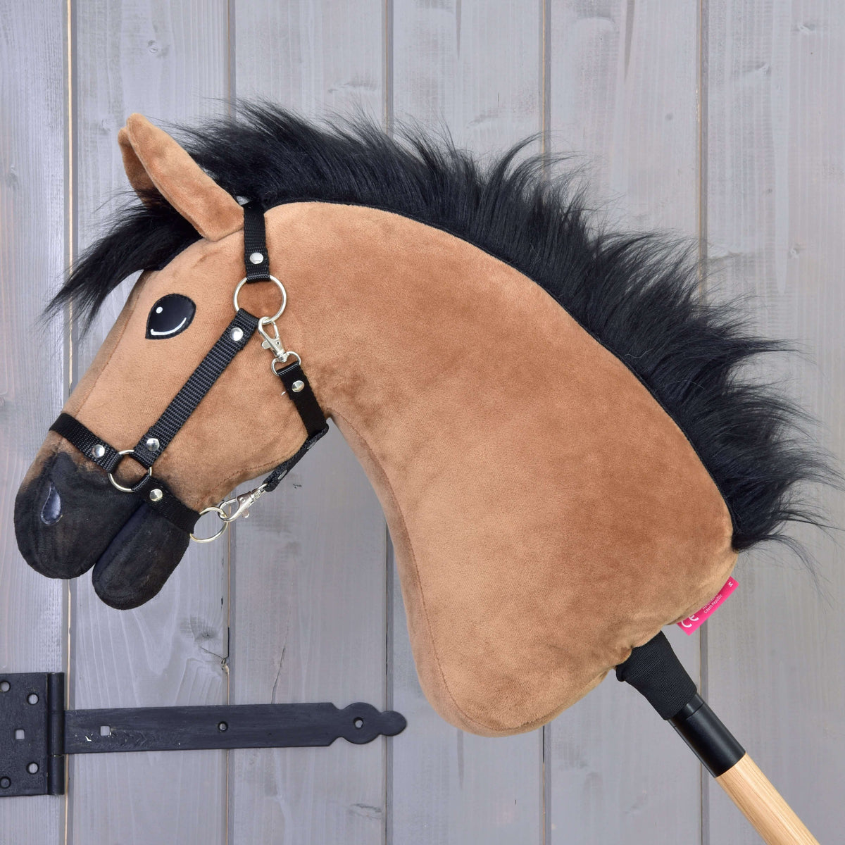 Zijaanzicht van de lichtbruine Hobby Horse met pluizige zwarte manen, zwarte neus en zwart halster op een stok