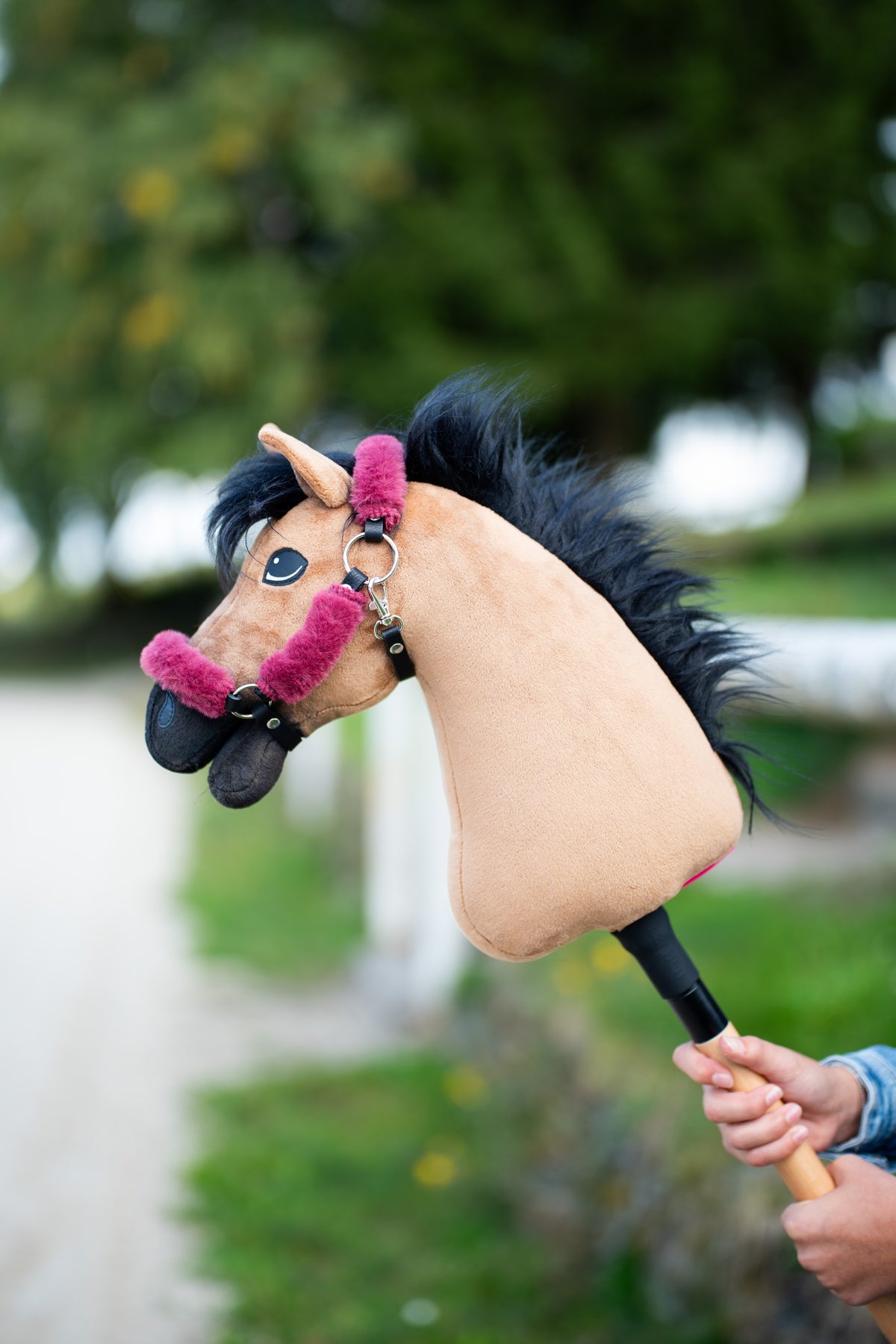 Hobby Horse Cookie met zwart halster met frambooskleurig bont en ruige zwarte manen, omhooggehouden voor bomen