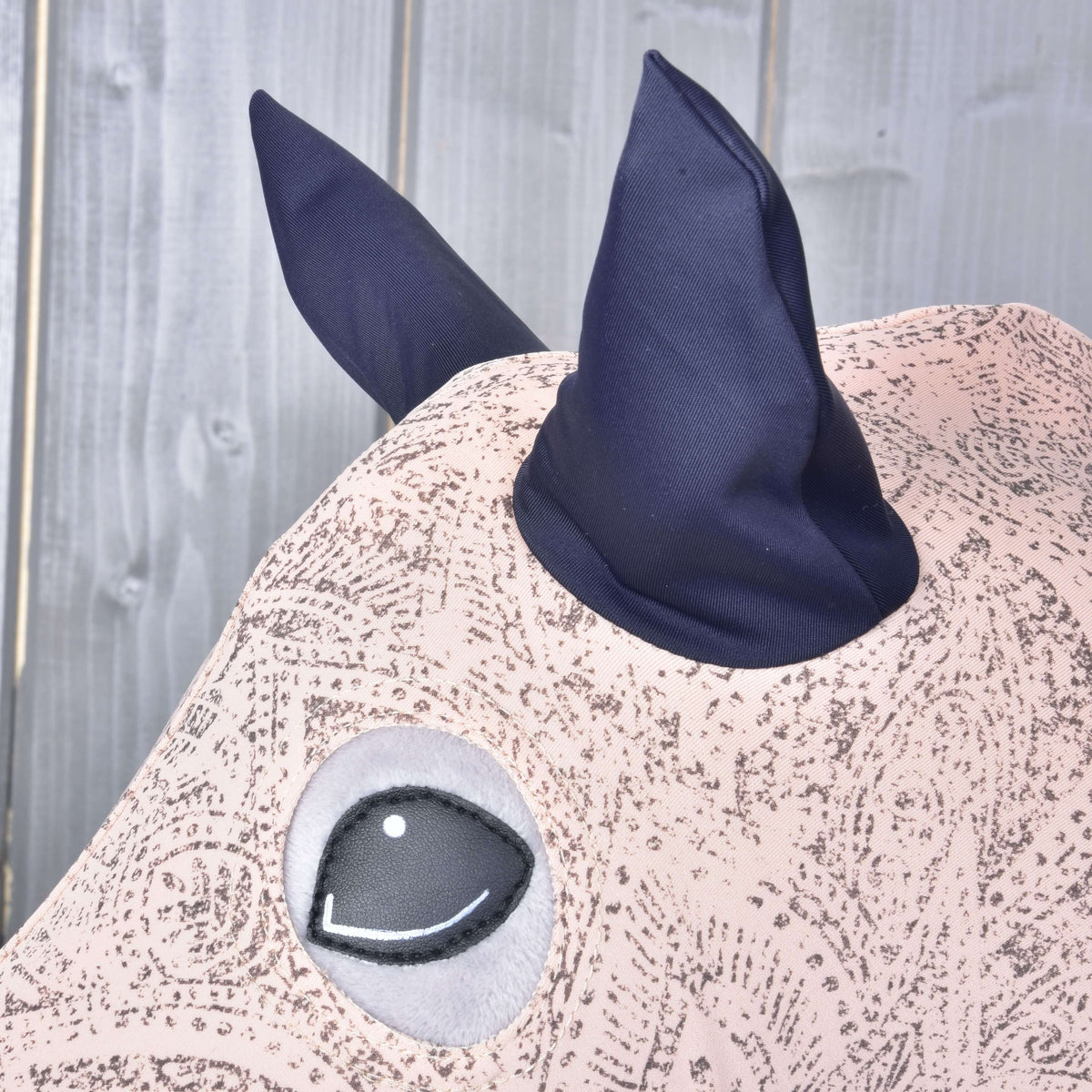 Close-up van de marineblauwe oren en de ronde oogopening van het roze Lycra-pak met paisleyprint op een grijze Hobby Horse