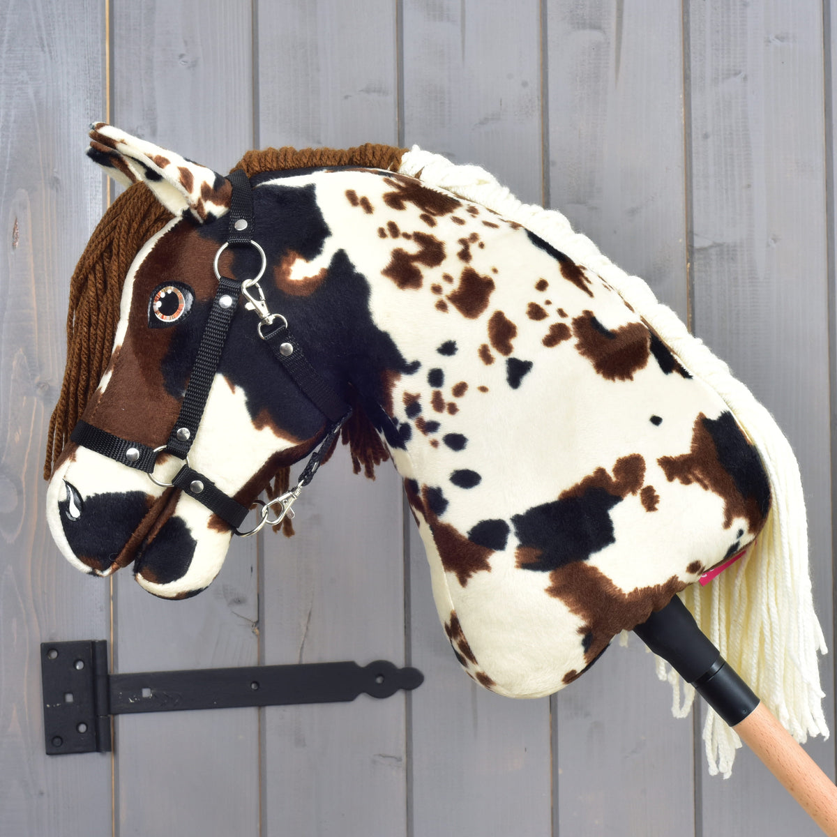 Hobby Horse Dakota avec licol noir de profil gauche, encolure crème tachetée et crinière en fil crème à l’arrière