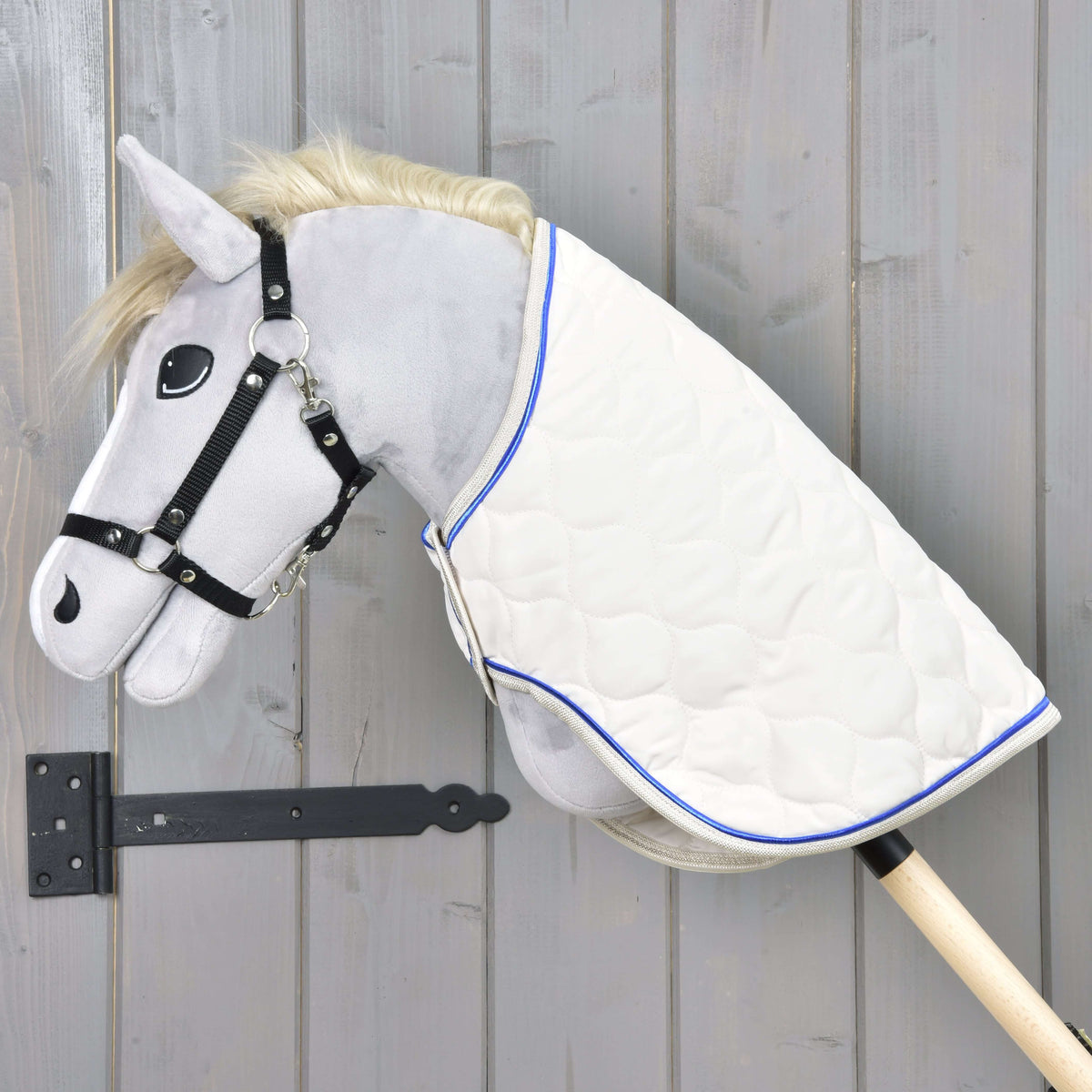 Grijze Hobby Horse met zwart halster draagt de Deken Cream Pearl, crème gewatteerd met koningsblauwe bies, over de hals