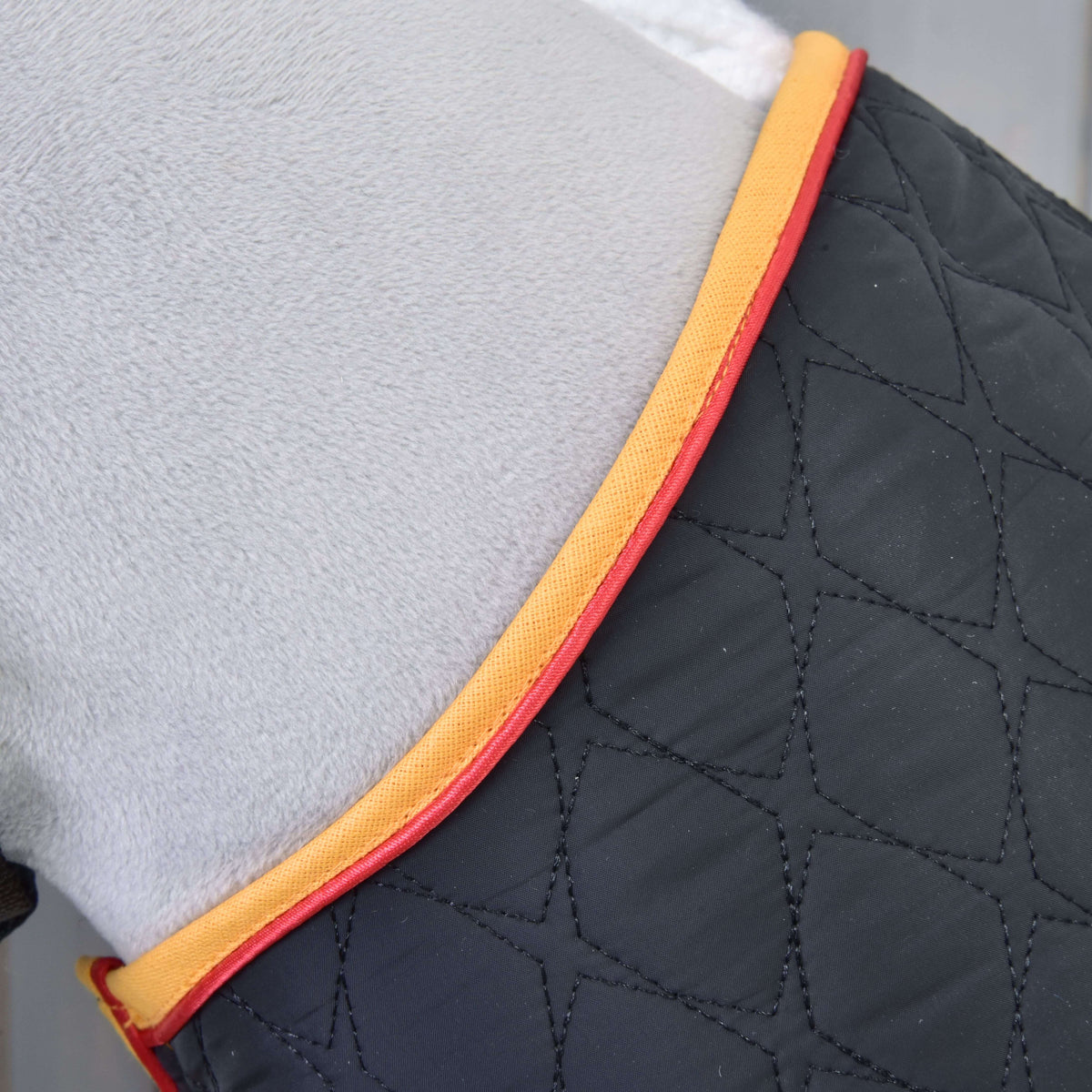 Close-up of the black diamond quilting with gold binding and red piping along the neckline on grey plush