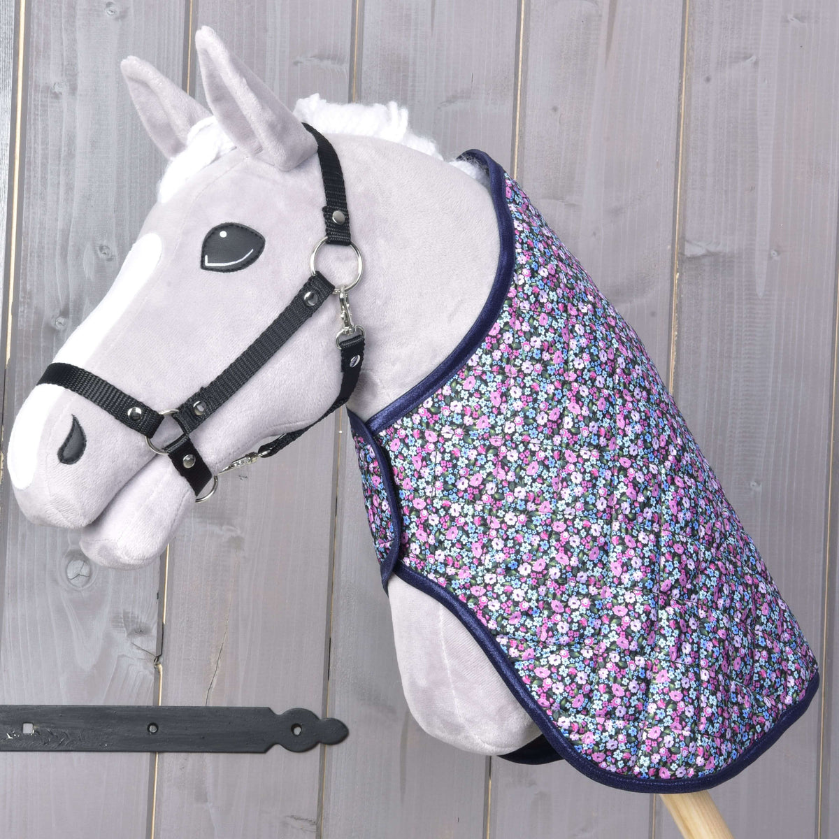Hobby Horse gris avec licol noir portant la couverture matelassée fleurie bordée de bleu marine sur l’encolure