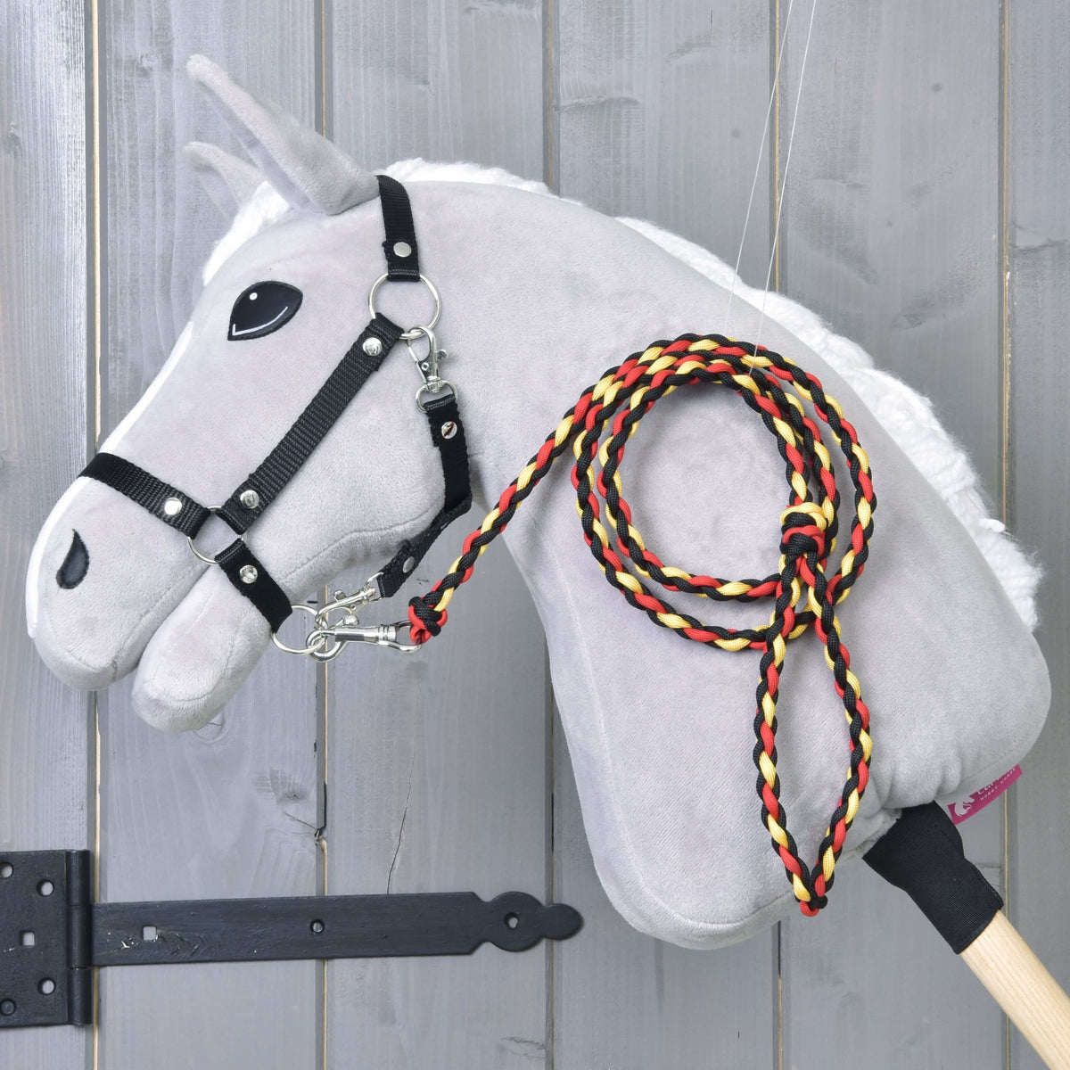 Lichtgrijze Hobby Horse met zwart halster en het gevlochten zwart-rood-gele halstertouw Flag over de hals