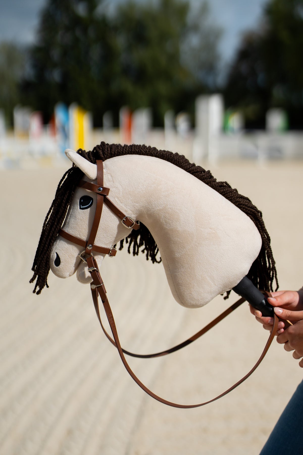 Cream Hobby Horse Frederik LD with a dark brown yarn mane in the brown bridle with noseband and long reins, jumps behind