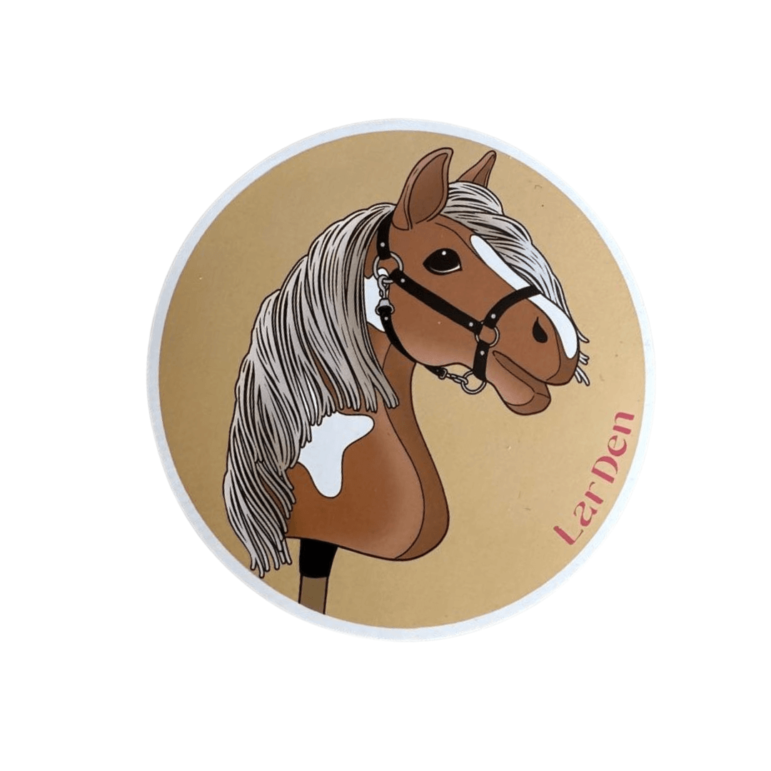 Sticker met een bruin-witte bonte Hobby Horse met lange grijze manen en zwart halster op een zandkleurige cirkel