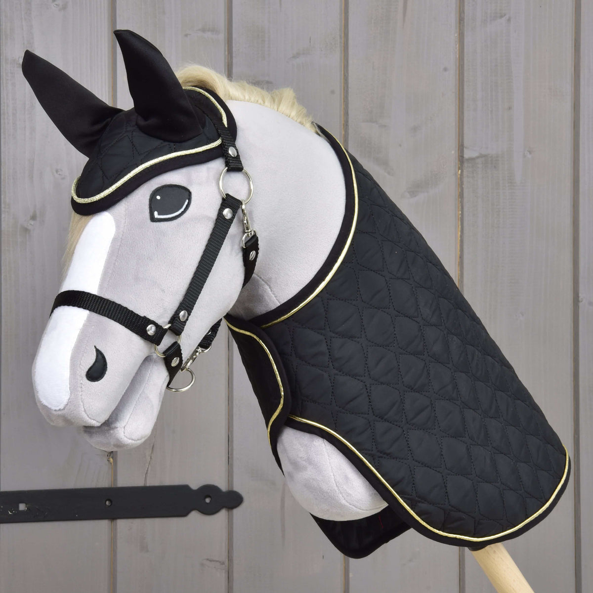 Grijze pluche Hobby Horse met zwarte halster in de zwarte doorgestikte deken en het oornetje met gouden bies