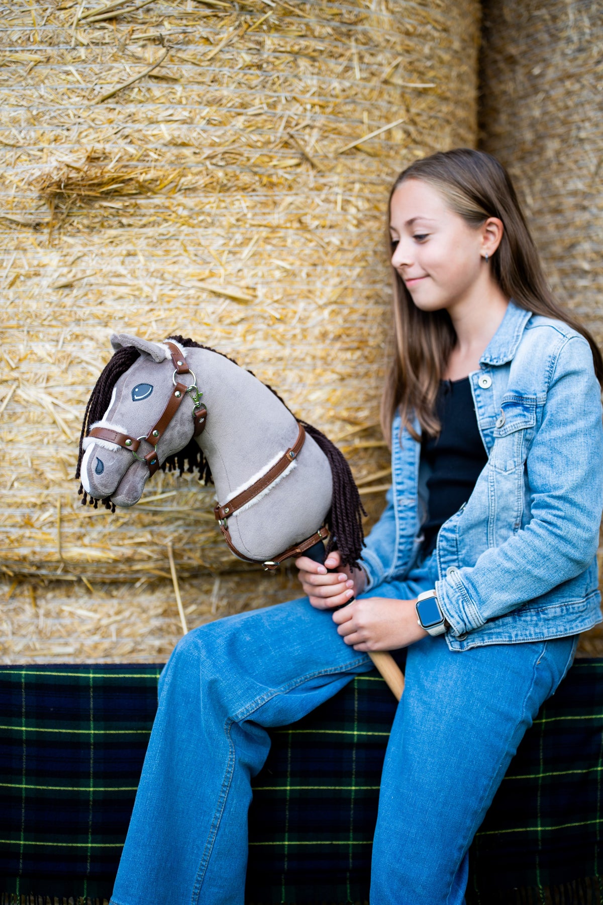 Meisje in spijkerjasje op strobalen met Hobby Horse Guccini in bruine halster met bont en bijpassend borsttuig