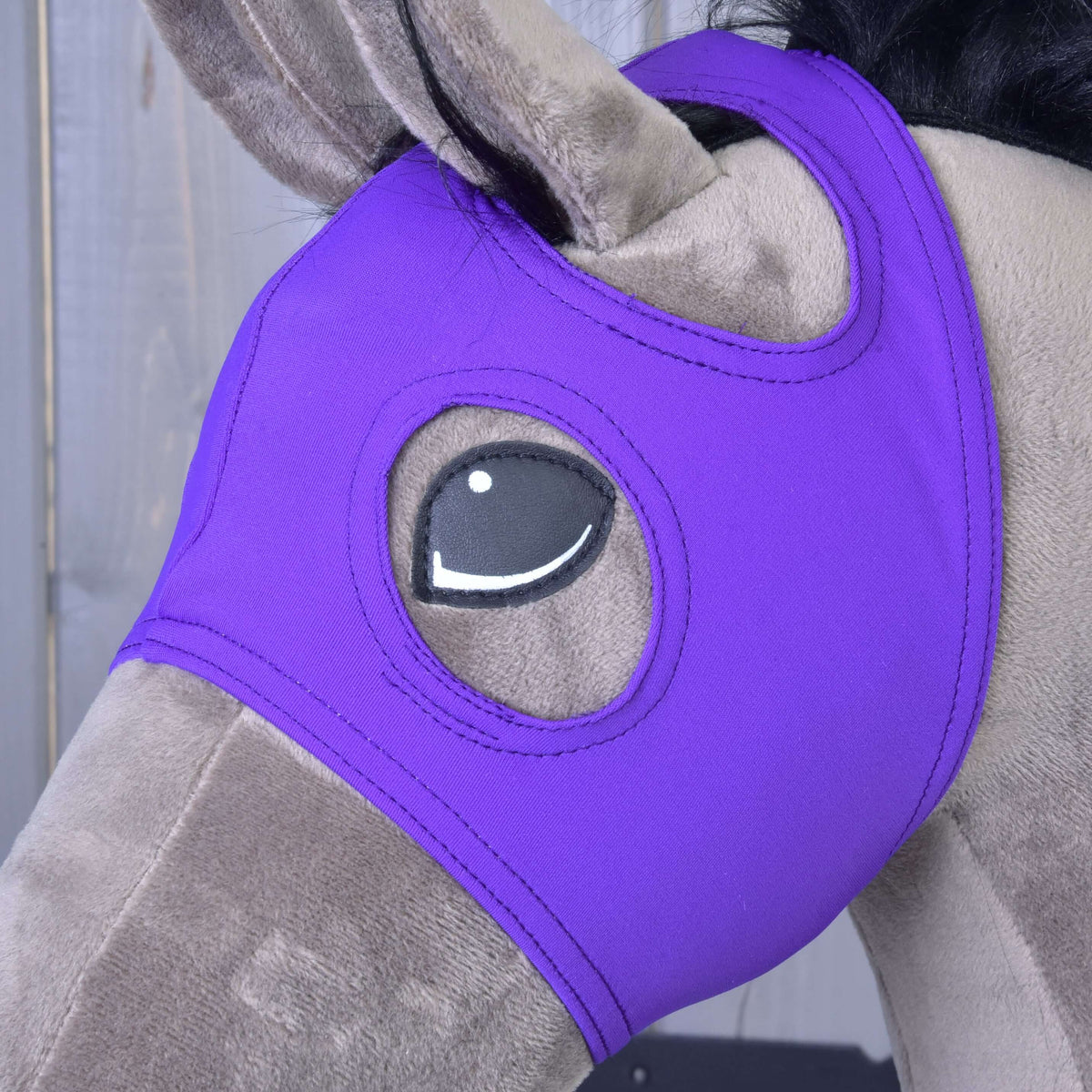 Gros plan sur le masque violet sur un Hobby Horse gris-brun, l’oreille passée dans son ouverture et l’œil dans une ouverture surpiquée