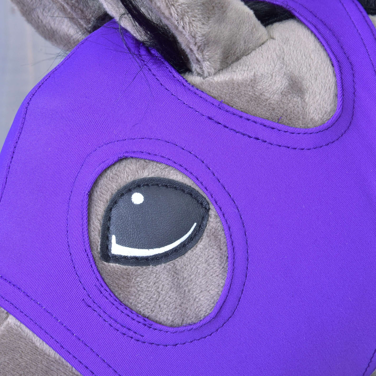 Détail de l’ouverture pour l’œil soigneusement surpiquée dans le tissu extensible violet du masque Indigo, autour de l’œil d’un Hobby Horse