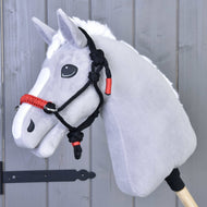 Grijze pluche Hobby Horse met witte manen en de zwart-rode touwhalster voor een grijze houten wand
