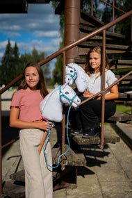 Deux filles sur un escalier métallique avec des Hobby Horses blancs en licols bleu pastel, l’un avec une longe bleue tressée