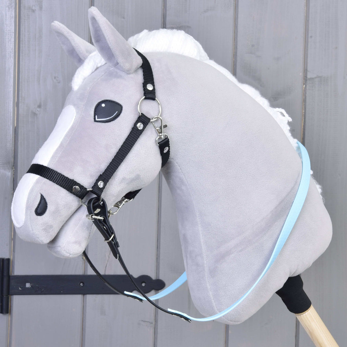 Hobby Horse van grijs pluche met zwarte halster en lichtblauw-zwarte gerubberde teugels vastgegespt onder de kin