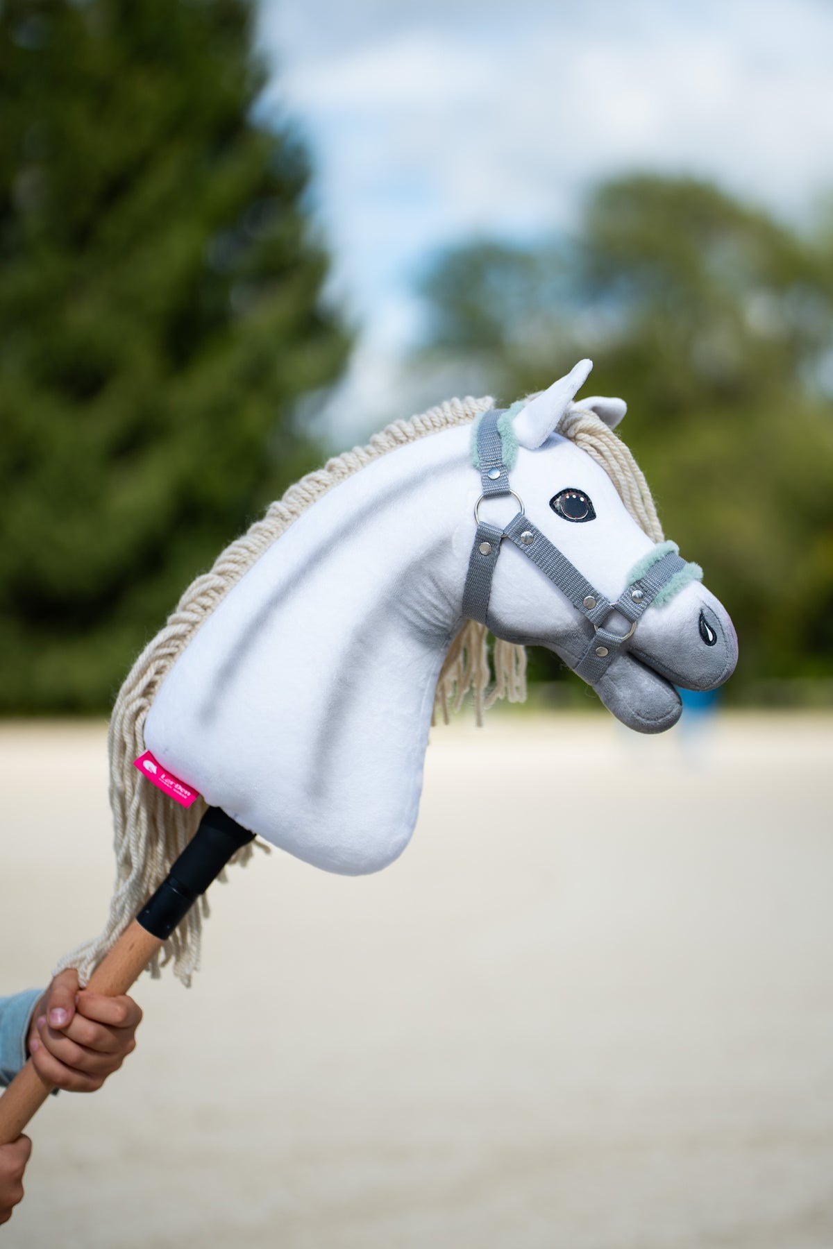 Witte Hobby Horse Little Lady met grijze schaduw en crème manen in het grijze halster met mint bont, omhooggehouden voor bomen