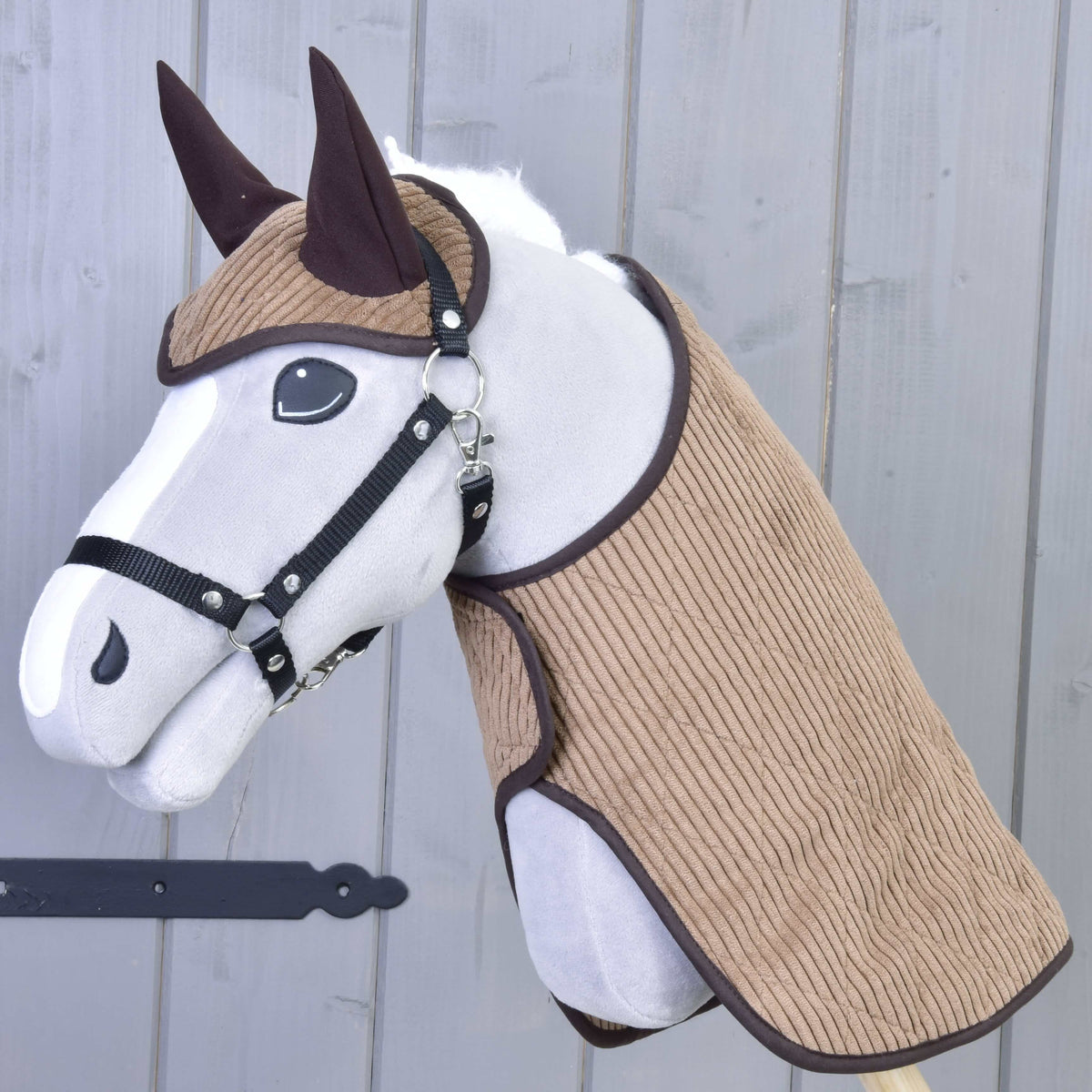 Hobby Horse gris avec licol noir portant la couverture et le bonnet d’oreilles en velours côtelé brun clair bordés de brun foncé