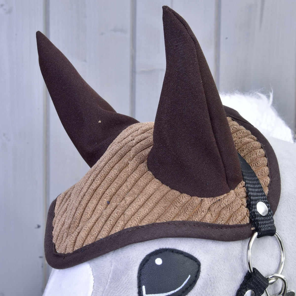 Gros plan sur le bonnet d’oreilles en velours côtelé brun clair aux oreilles et bordure brun foncé sur un Hobby Horse gris