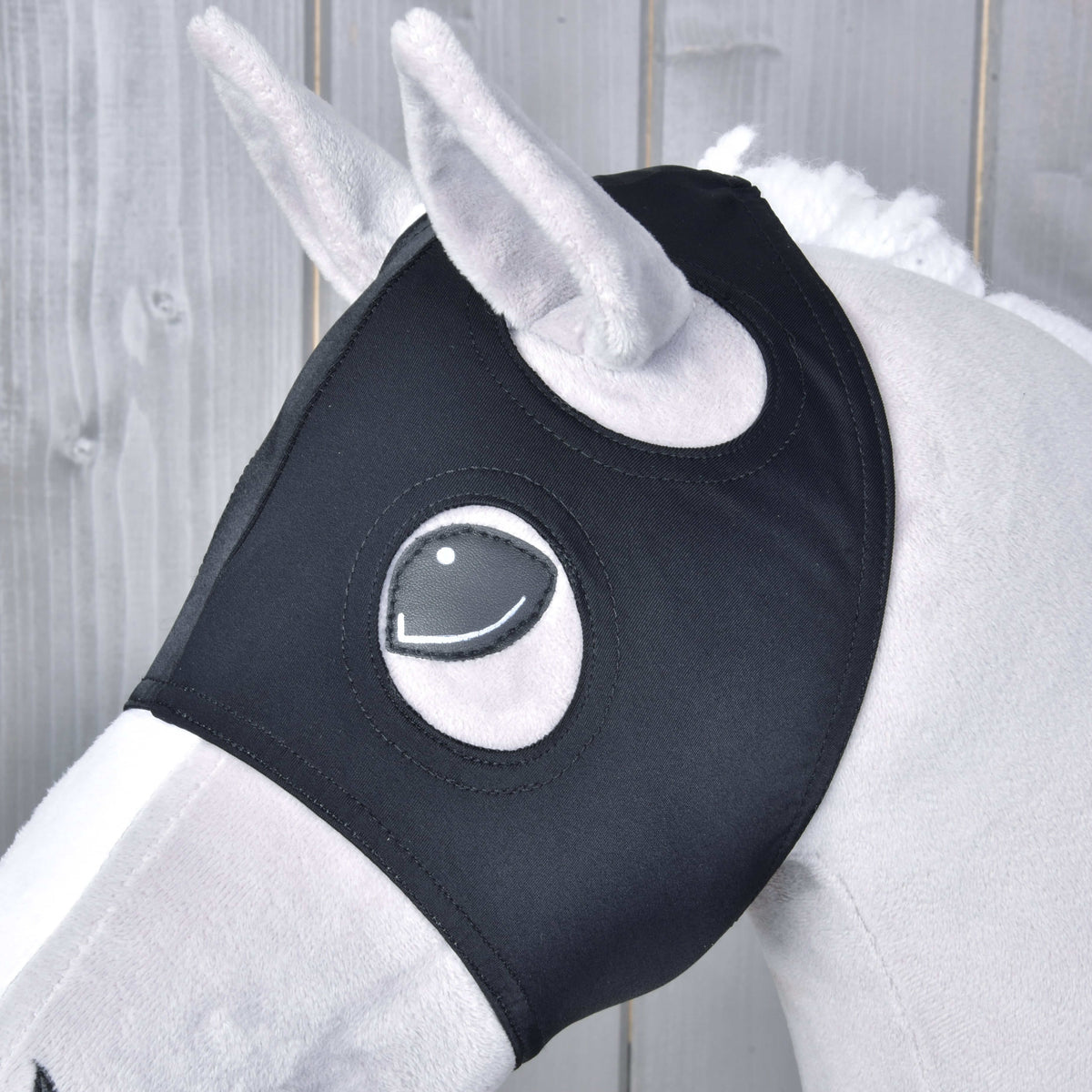 Close-up van het zwarte masker op een grijze Hobby Horse, het pluche oor en het gestikte oog steken door de ronde openingen